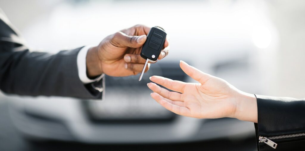 Car salesman handing over keys for new car to young woman